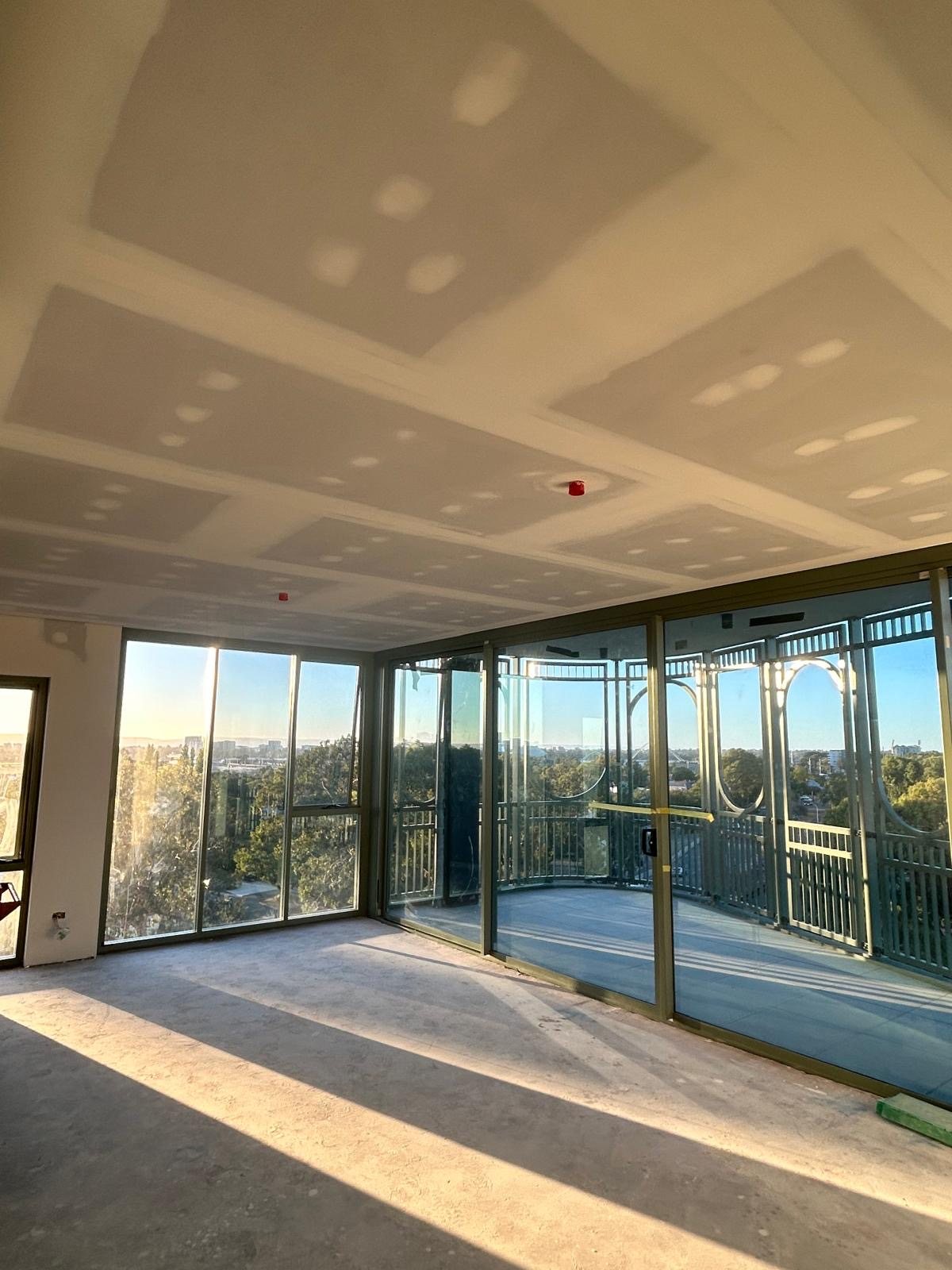 Apartment living area with set ceilings and flushed linings, corner glazing beyond.
