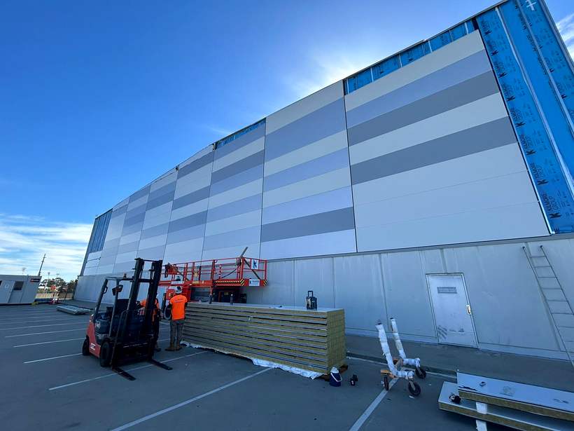 Cladding panels part-installed with crew and materials at the base.