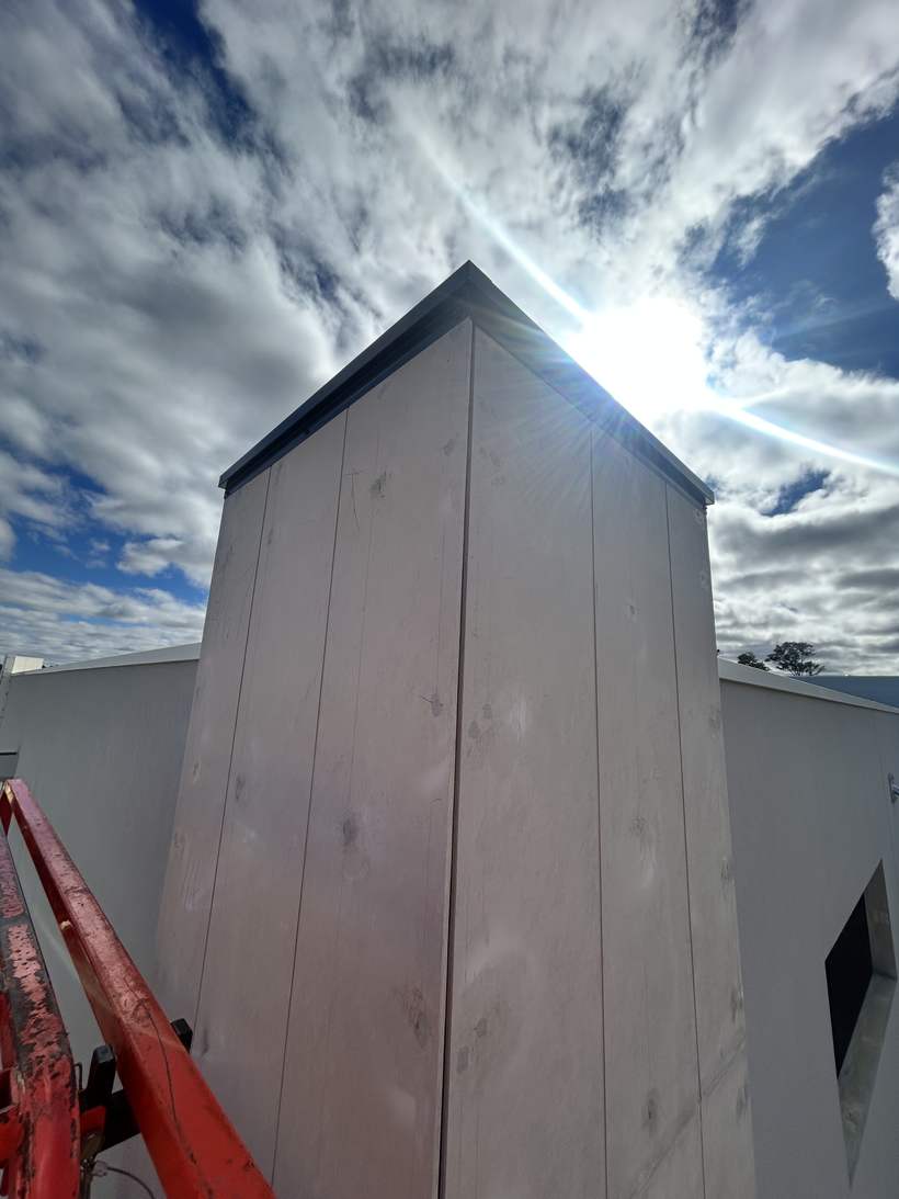 Tall charcoal cladding blade against a rendered wall.
