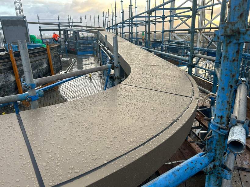 Curved halo capping running around the roof perimeter with scaffold alongside.